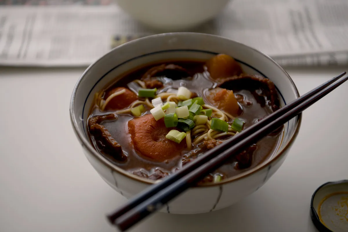 一碗門前隱味紅燒牛肉麵,上面有蔥花,旁邊放著筷子