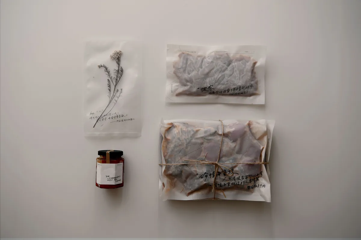 白色桌面上放著紙包好的門前隱味牛肉、一罐辣椒醬和手繪小卡