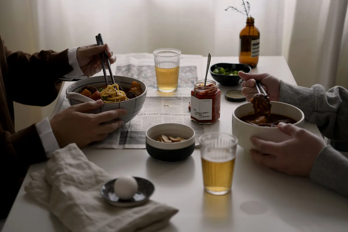 兩個人在餐桌上吃門前隱味牛肉麵,桌上有啤酒和小菜