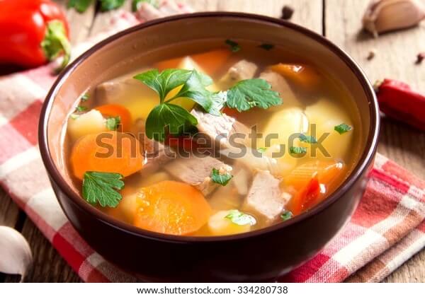 Meat and vegetables soup with parsley in bowl over rustic wooden background close up